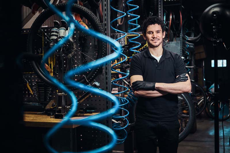 Young attractive mechanic is posing next to bicycle at his own workshop